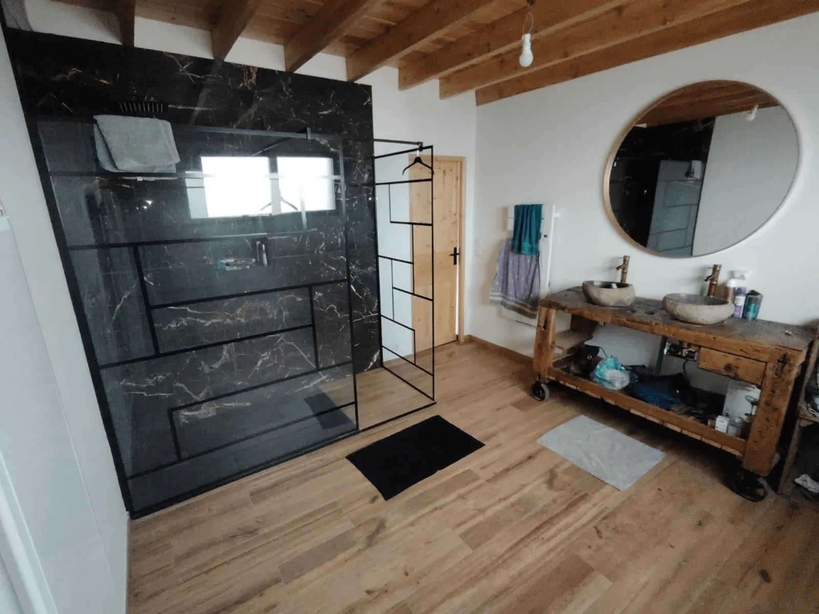 Salle d’eau avec paroi de douche noire, carrelage aspect marbre et meuble vasque en bois