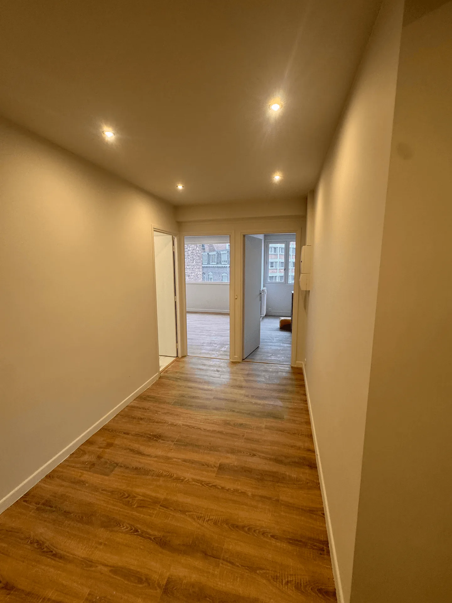 Couloir aux murs clairs, sol aspect bois et spots au plafond