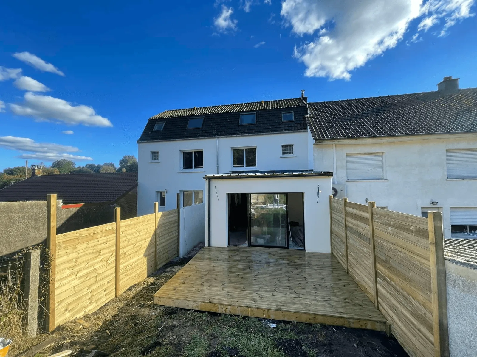 Extension enduite avec baie vitrée et terrasse en bois, abords en terre