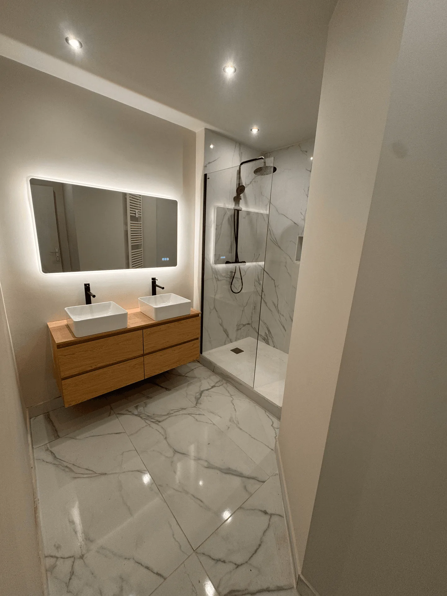 Salle de bain avec double vasque, miroir éclairé et carrelage aspect marbre